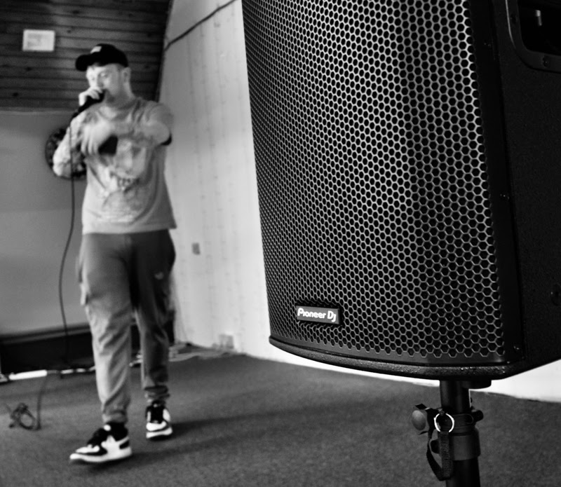 Artista de hip hop actuando en el Crosville junto a un altavoz Pioneer DJ XPRS2 en primer plano (imagen en blanco y negro).