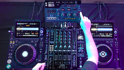 AlphaTheta RMX-IGNITE integrado en una cabina DJ profesional con reproductores y mesa de mezclas